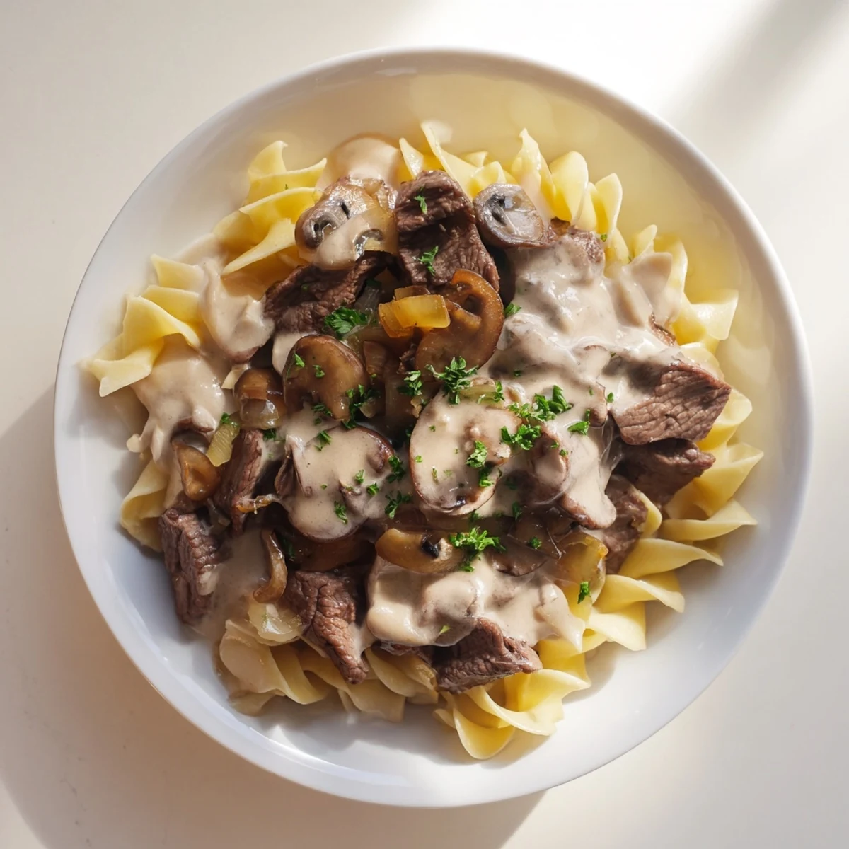 Sizzling strips of beef and cremini mushrooms simmer in a creamy, savory sauce, ready to be spooned over tender egg noodles for a comforting Beef Stroganoff dinner. 