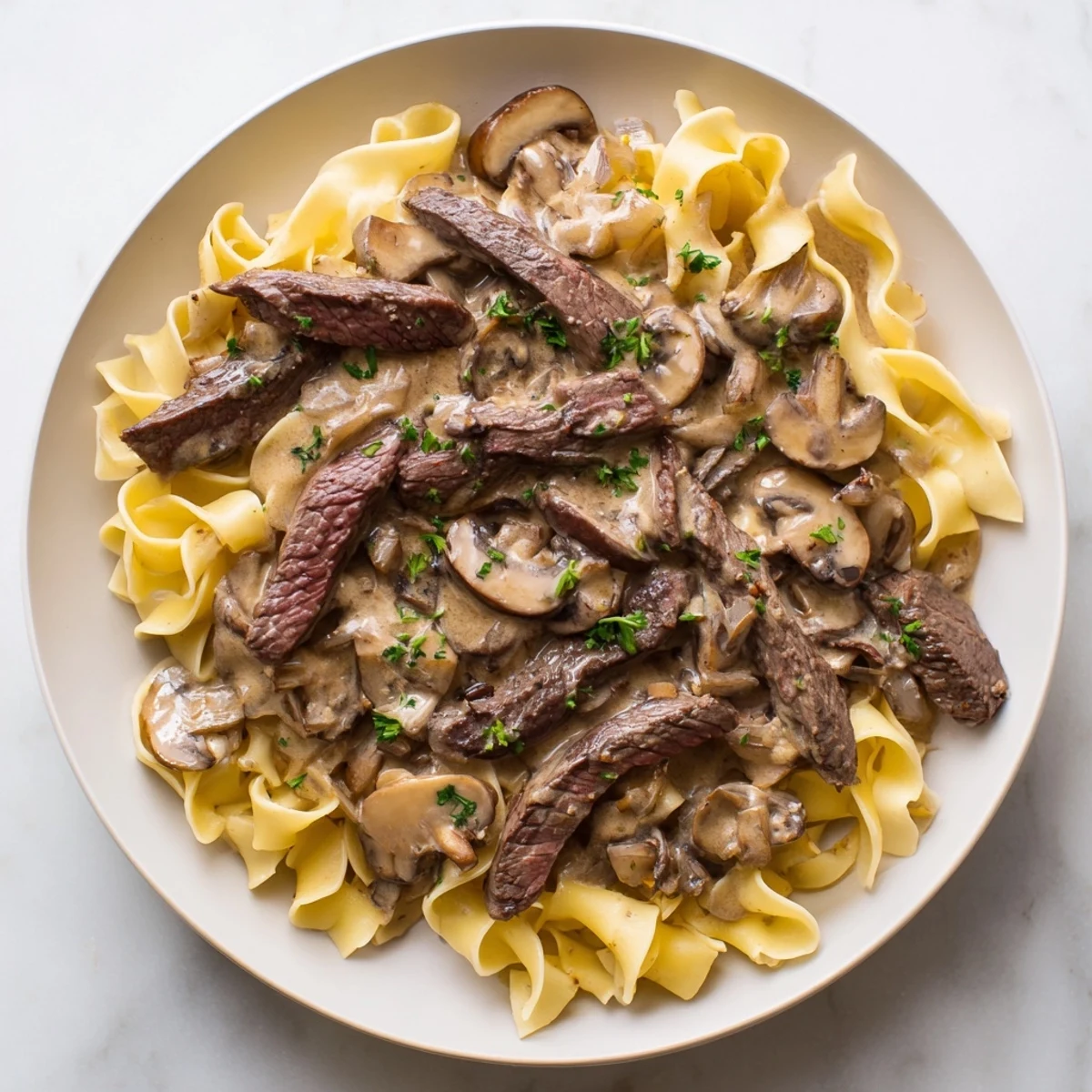 A rustic cast-iron skillet serves steaming Beef Stroganoff over buttery egg noodles, garnished with bright parsley, alongside fresh green beans on a wooden table.
