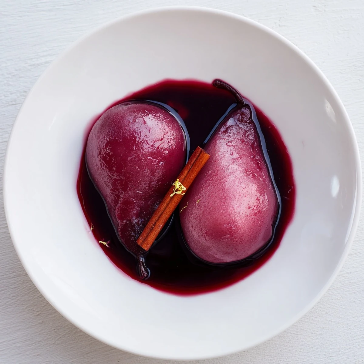 Golden Pears in Grape Juice, gently poached and glistening with a warm, cinnamon-infused syrup, served on a white plate.  