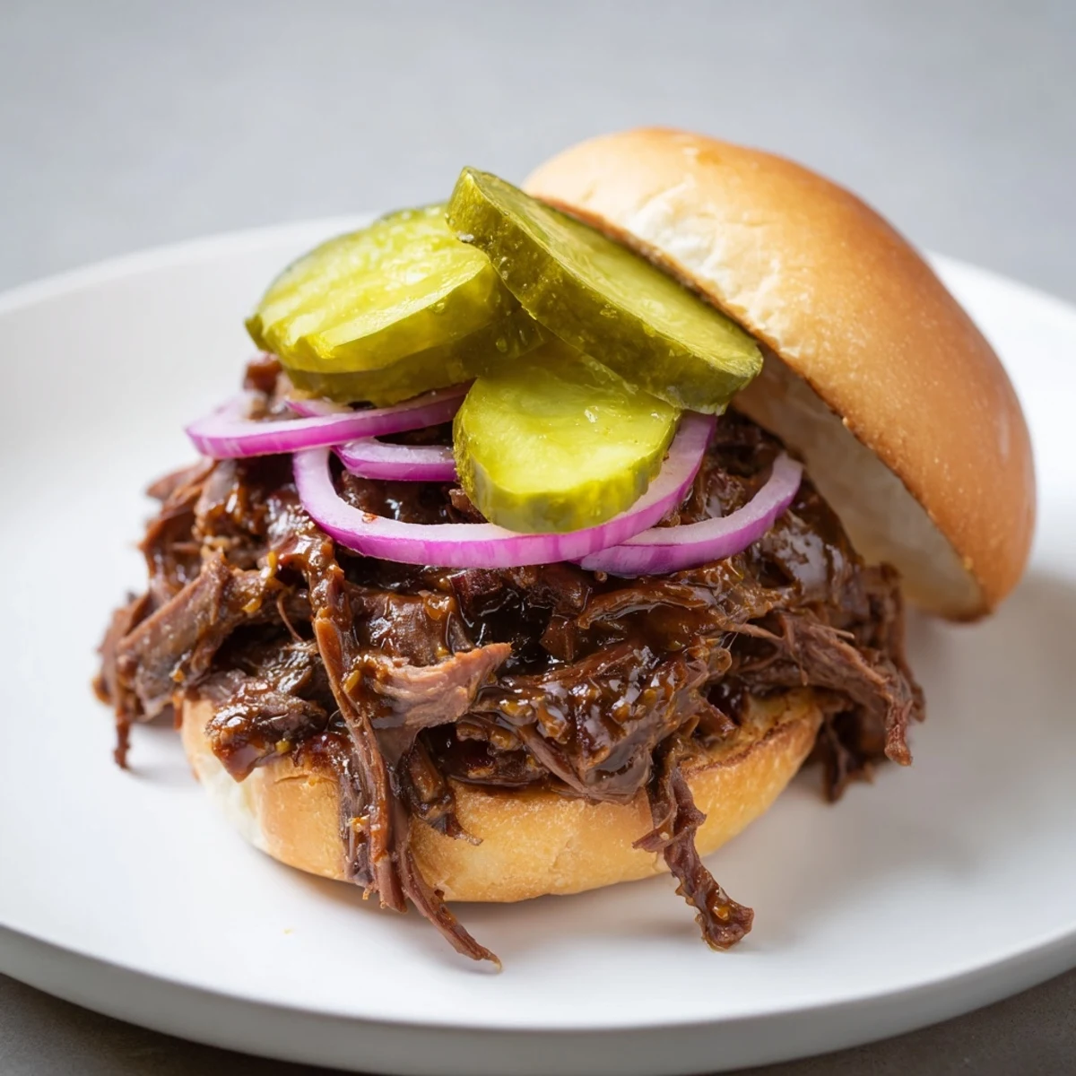 Golden-brown, shredded beef is piled high on a toasted slider bun, garnished with crisp red onion and tangy dill pickles.