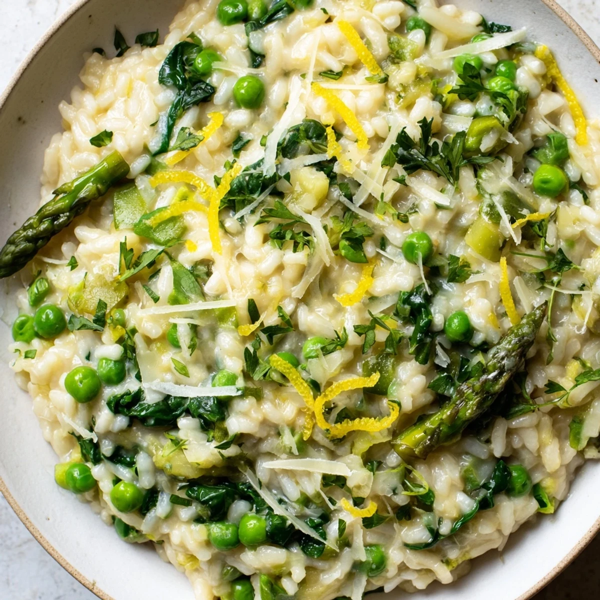 Spring Vegetable Risotto with Lemon Zest glimmers with creamy Arborio rice, green asparagus, peas, and bright lemon zest in a white ceramic bowl.