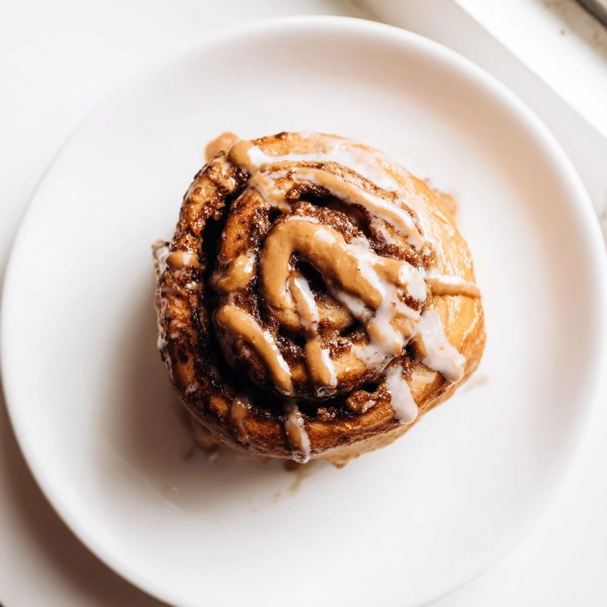 Warm Biscoff cinnamon rolls drizzled with glaze on a plate, ready to be enjoyed with a cup of coffee.