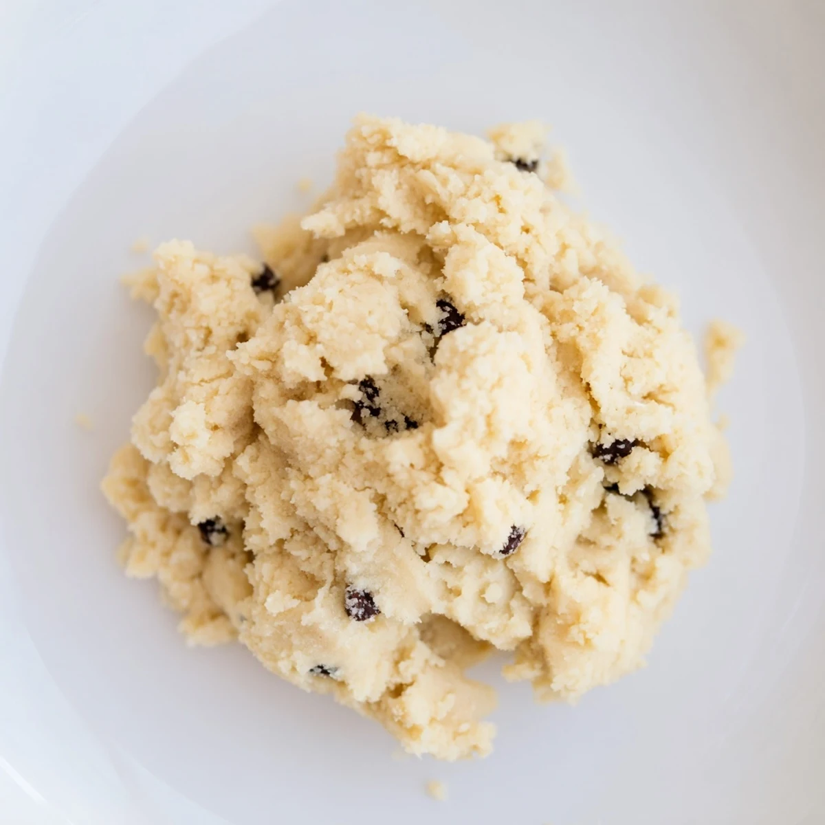 A close-up of creamy Edible Keto Cookie Dough in a bowl, topped with extra chocolate chips for a treat.
