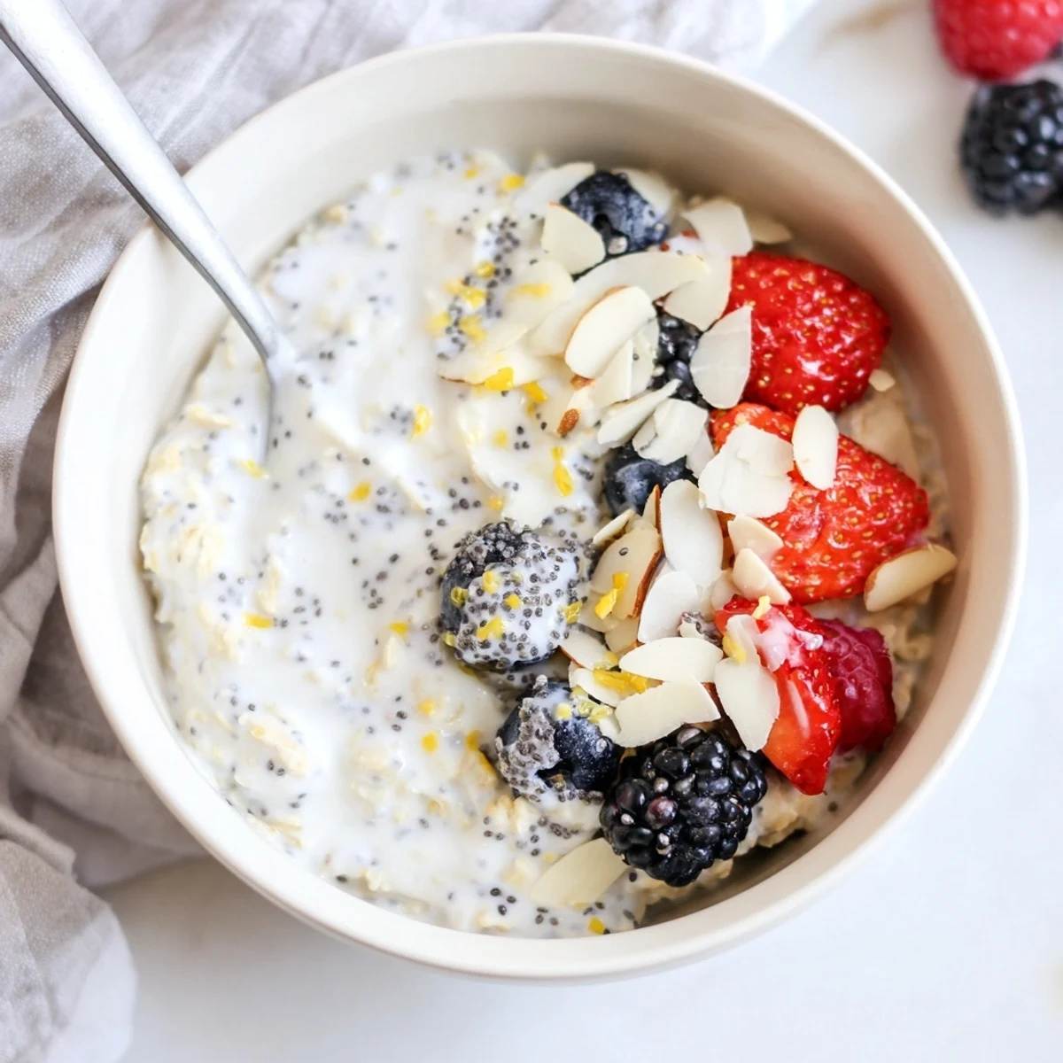 Vegan Lemon Poppy Seed Overnight Oats served chilled in a white bowl with almond slices and a drizzle of maple syrup.