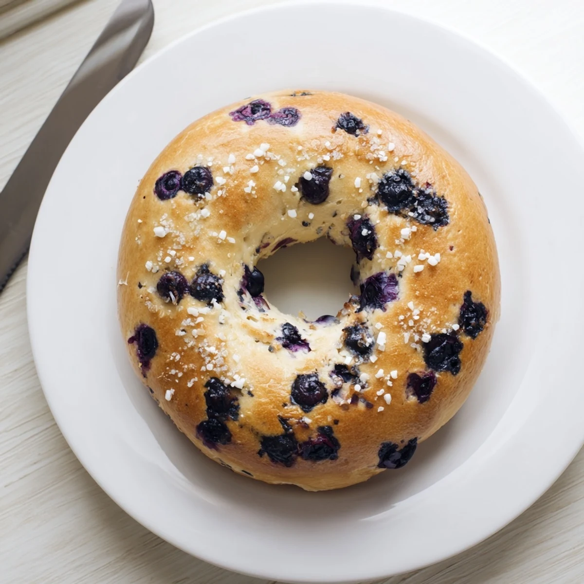 Gluten-Free Blueberry Bagels on a wire cooling rack with coarse sugar topping, next to a schmear of cream cheese and a cup of coffee.