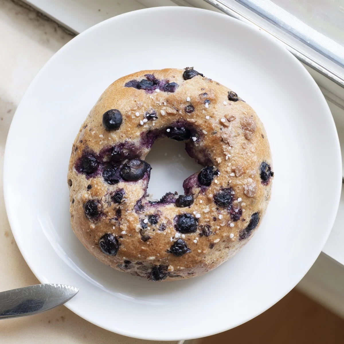 A close-up of a fresh, gluten-free blueberry bagel with a golden crust, glistening egg wash, and bursting blueberries, perfect for a gluten-free breakfast.