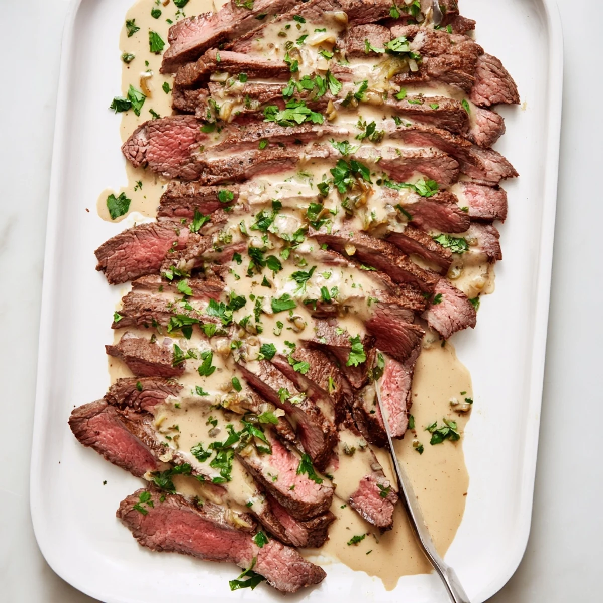 Golden-brown roasted garlic cloves nestled beside sliced flank steak draped in a velvety sauce, garnished with fresh parsley.