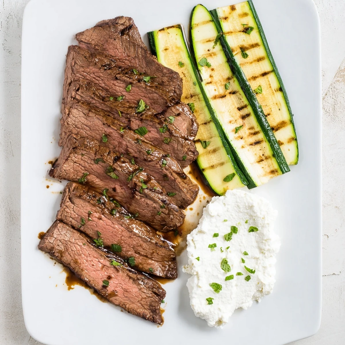 Sliced Balsamic Flank Steak With Grilled Zucchini And Whipped Feta garnished with fresh mint on a summer table setting.