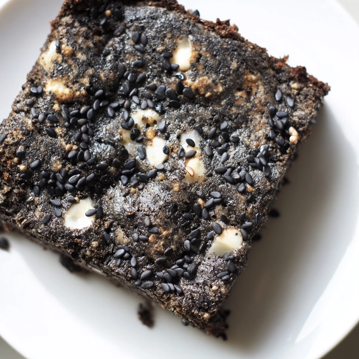 A close-up of freshly cut Black Sesame Blondies, showcasing their rich, nutty crumb and buttery edges on a wooden board.