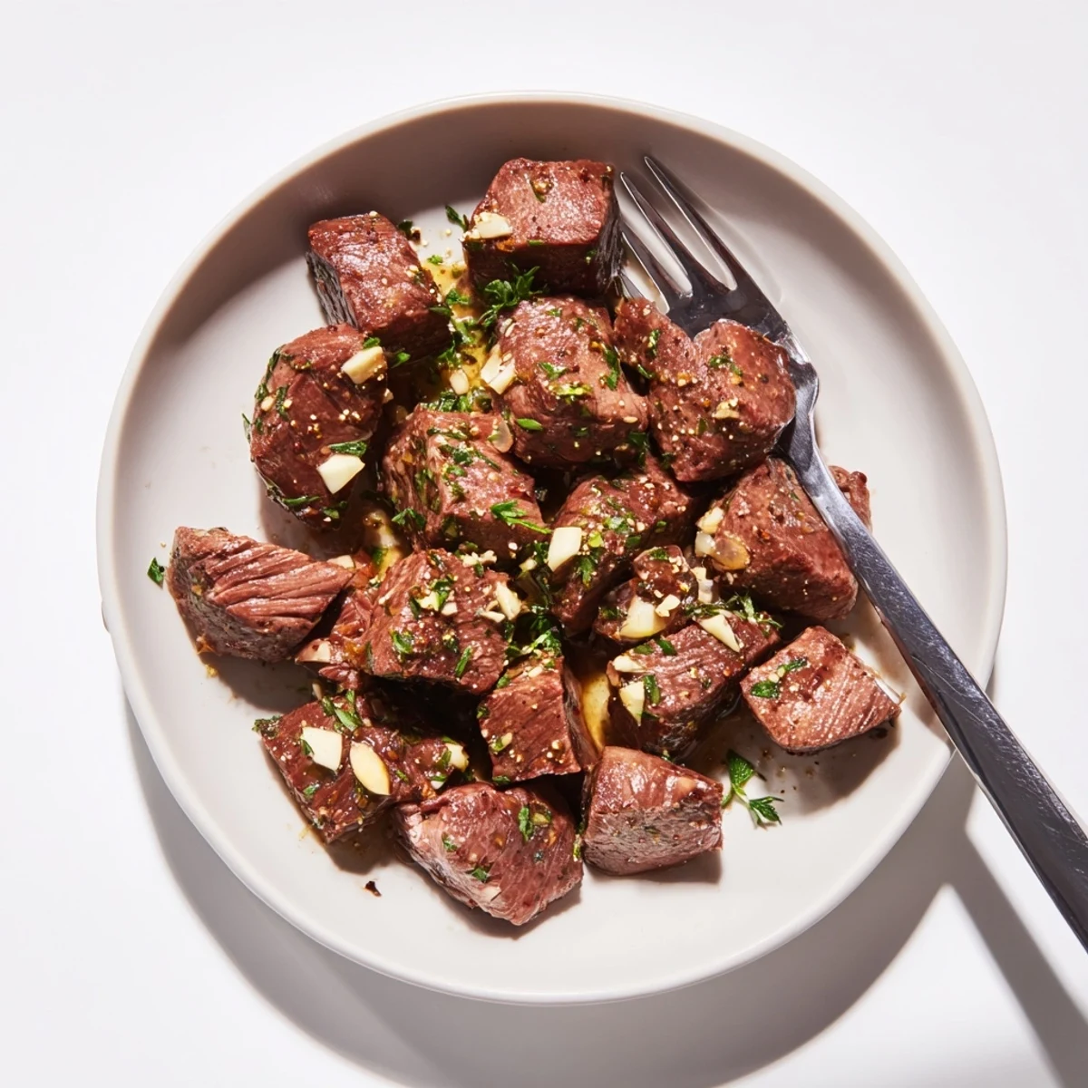 Succulent seared steak bites coated in buttery garlic glaze served on a white plate