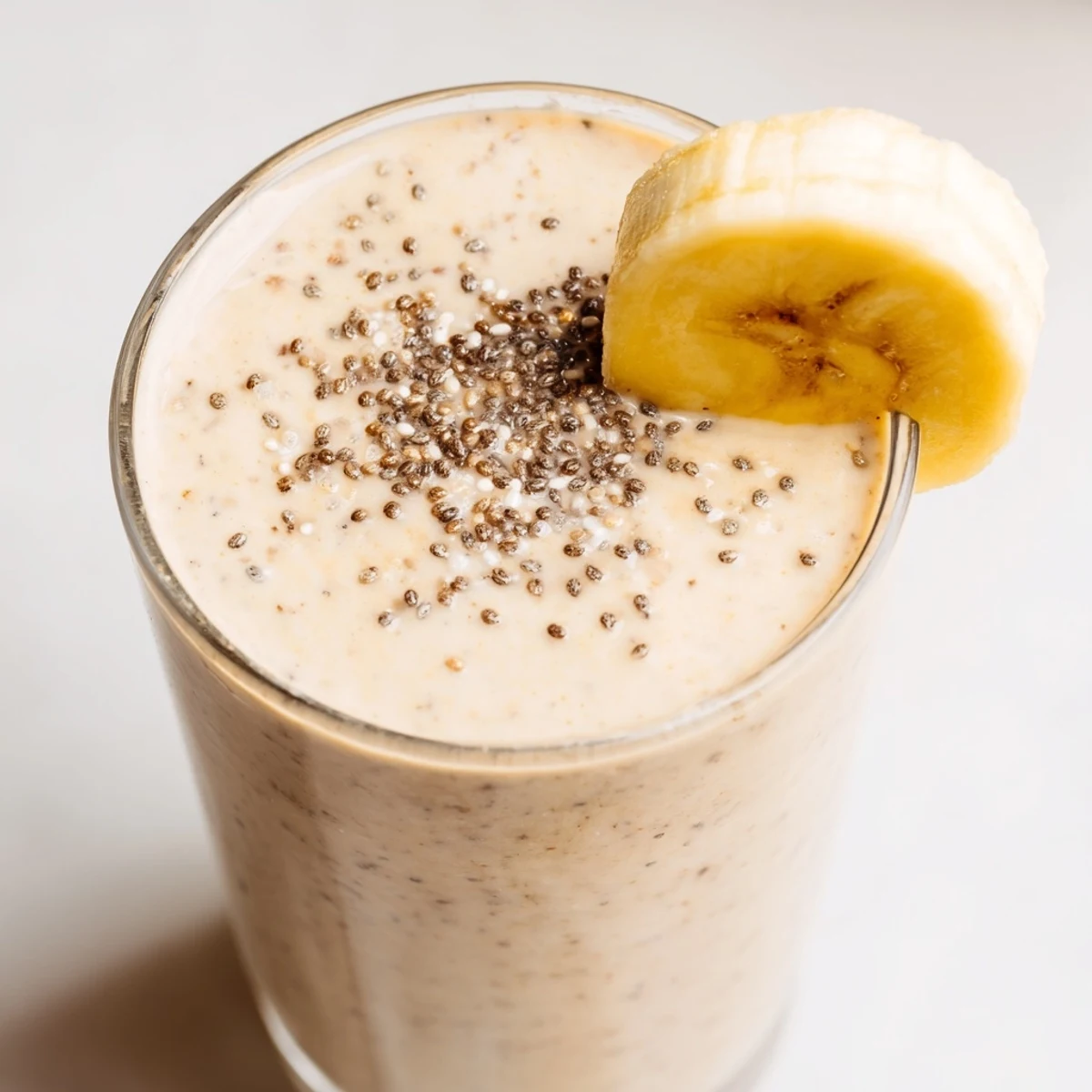 Creamy Greek yogurt banana smoothie poured into a tall glass with fresh banana slices on top