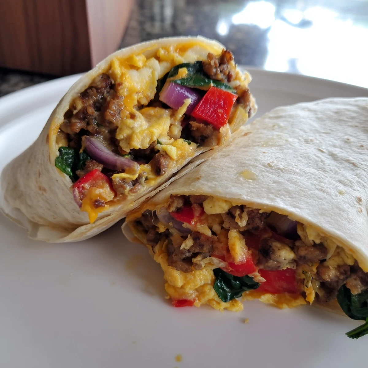 Plate of hearty make-ahead breakfast burritos filled with savory sausage, colorful peppers, and spinach