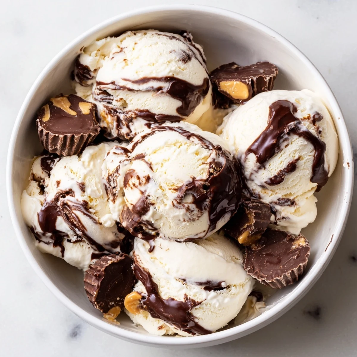 Rich vanilla homemade moose tracks ice cream featuring chocolate fudge ribbons and chopped peanut butter cups on a white background