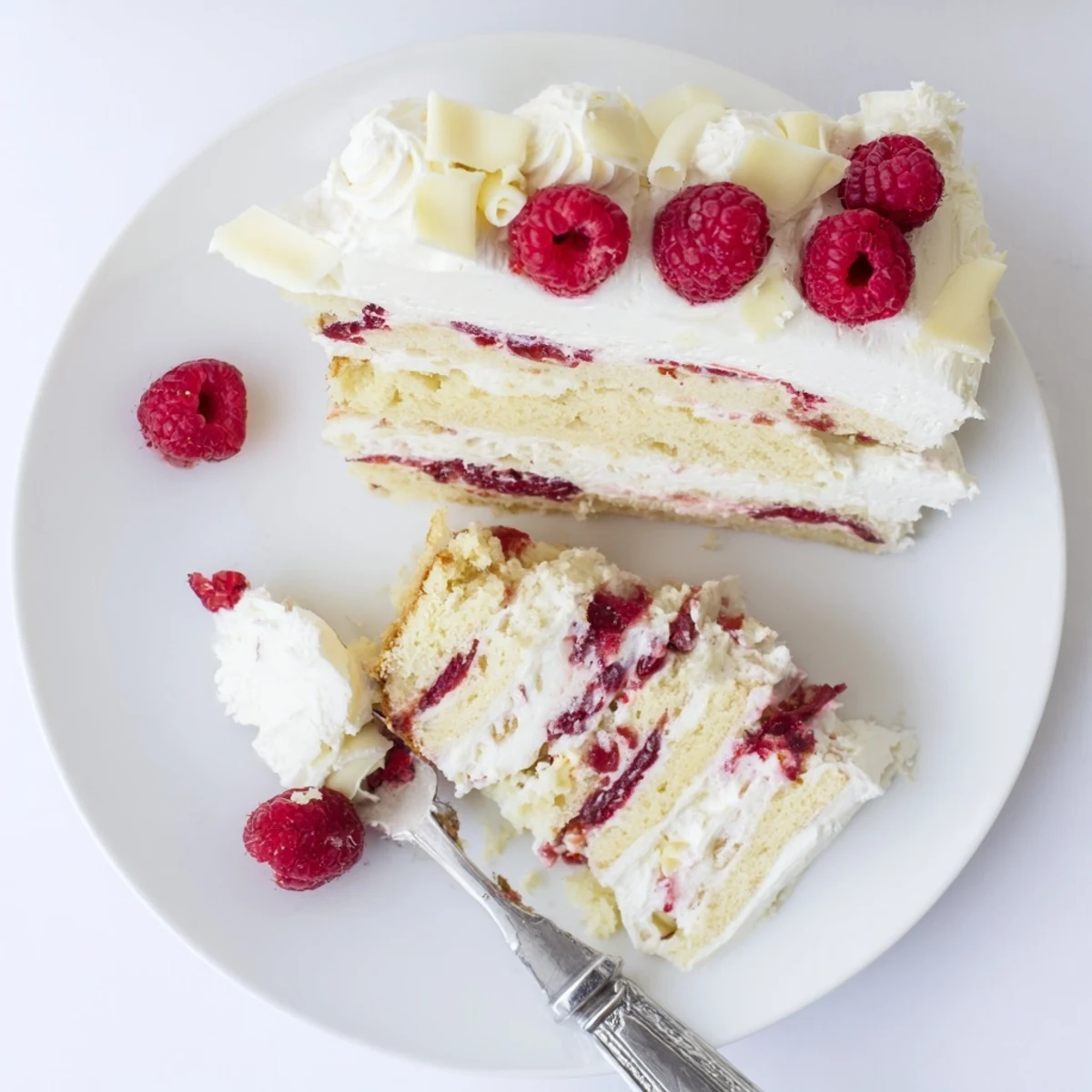 Three-tiered white chocolate raspberry cream cake displaying cross section of moist cake layers sandwiched between tangy raspberry filling and rich white chocolate cream