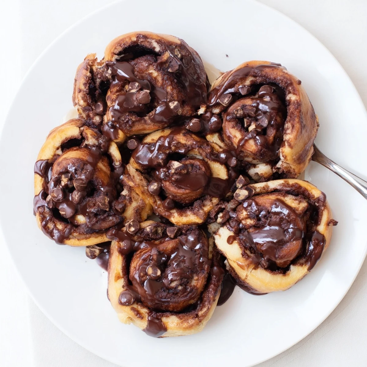 Freshly baked double chocolate cinnamon rolls drizzled with rich chocolate glaze on a white plate
