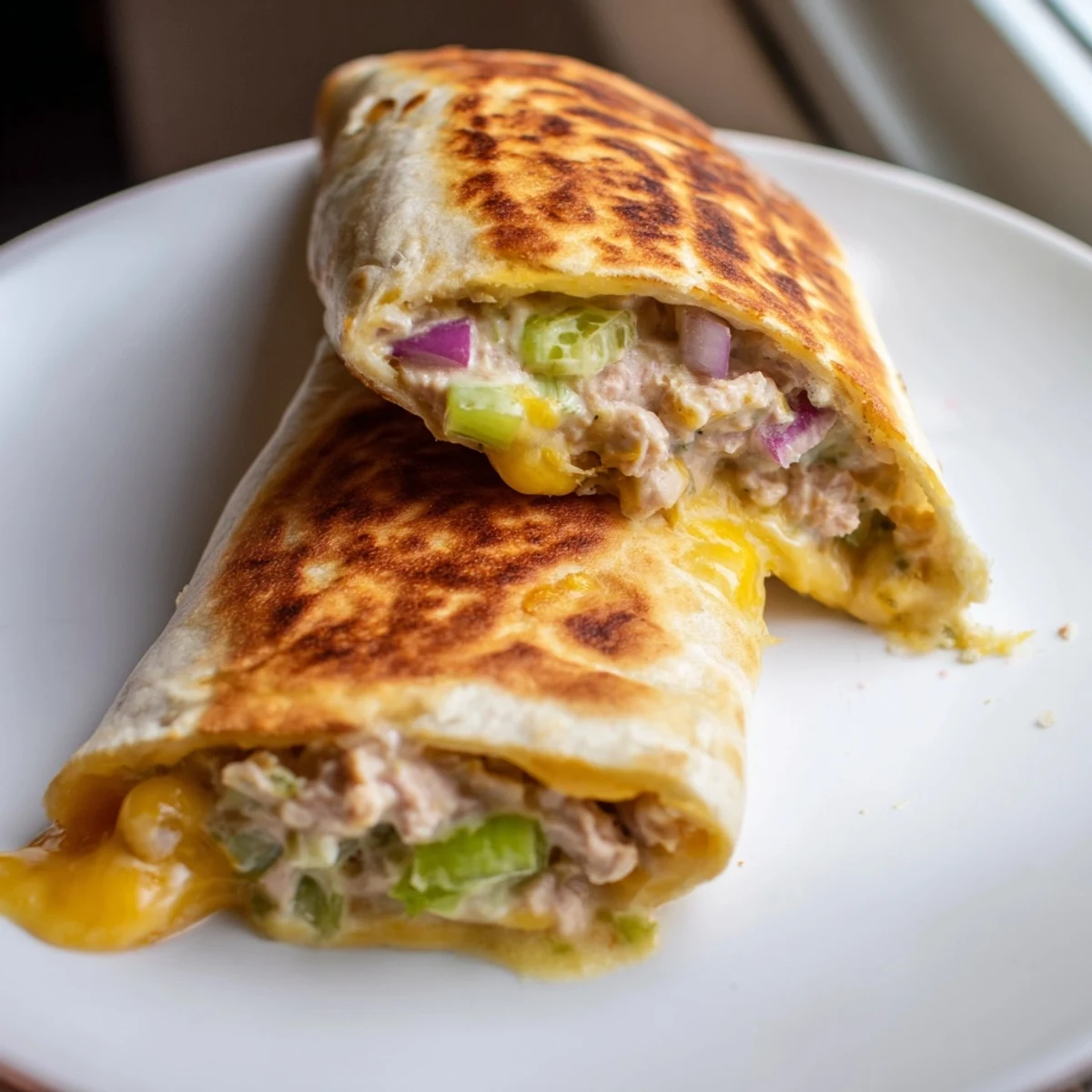 Tuna melt wrap cut diagonally on a white plate showing golden crispy tortilla and gooey cheese