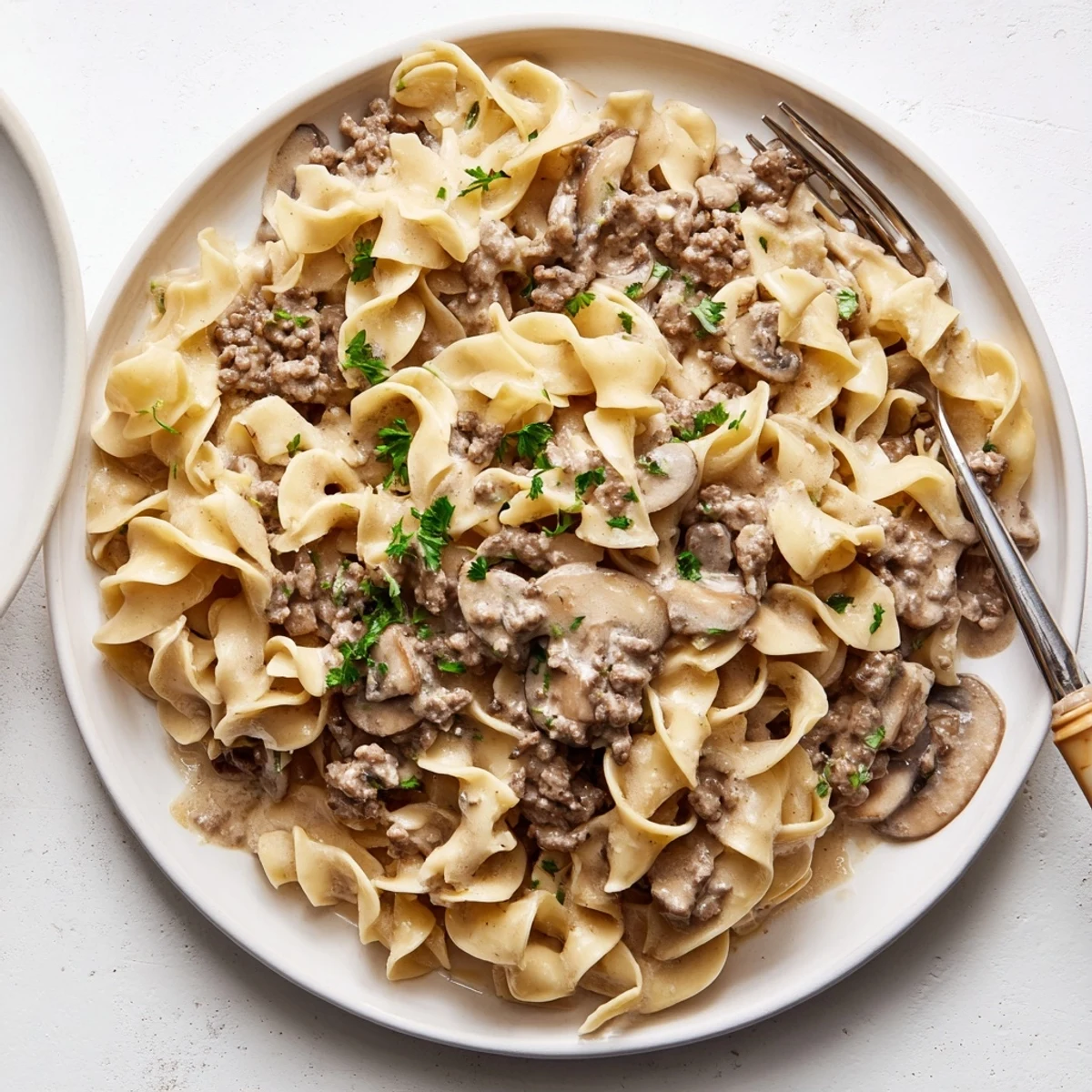 Hearty hamburger stroganoff plated over wide egg noodles with fresh parsley garnish