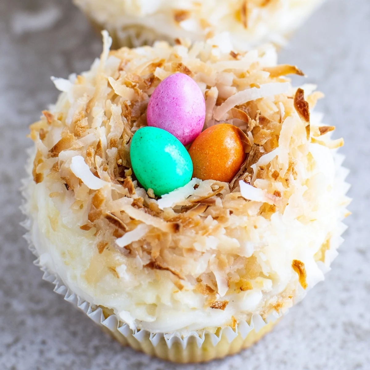 Easter-inspired vanilla cupcakes decorated with shredded coconut nests and candy chocolate eggs for festive spring desserts