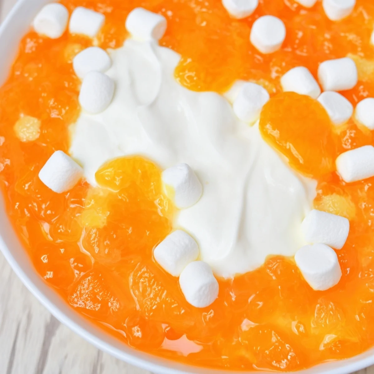 Festive orange gelatin dessert with pineapple and marshmallows served on a spring holiday table with fresh fruit garnish