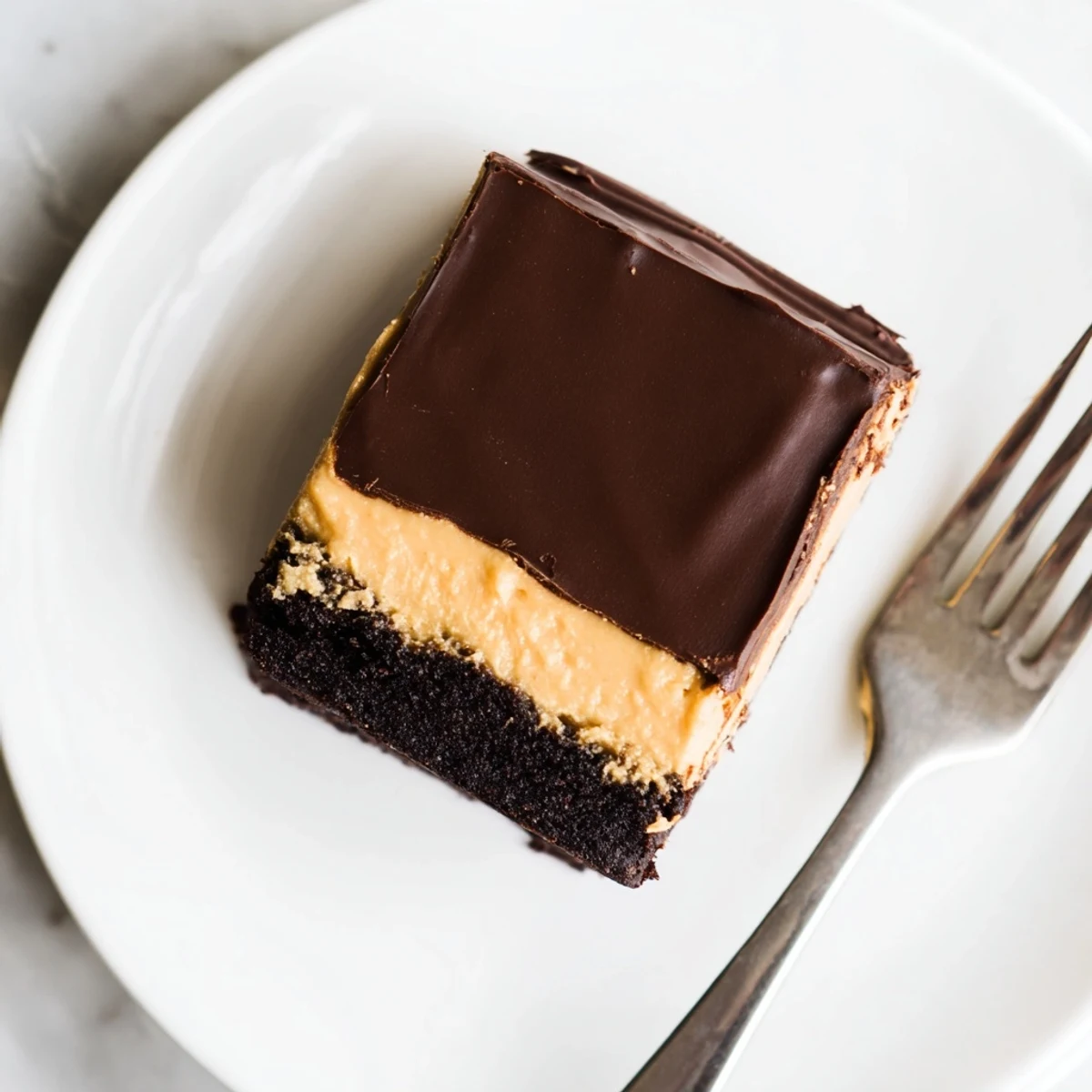 Homemade layered peanut butter brownies topped with glossy chocolate ganache on a white serving plate