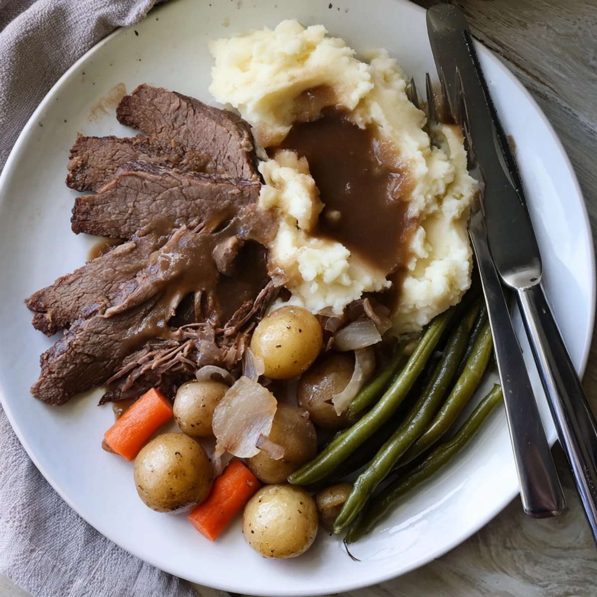 Fork-tender Southern style pot roast served on white plate with creamy mashed potatoes and seasoned green beans