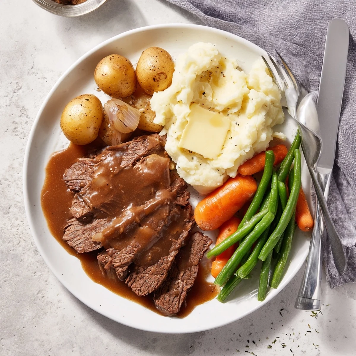 Slow-cooked Southern style pot roast with caramelized vegetables, brown gravy drizzled over mashed potatoes and crisp green beans