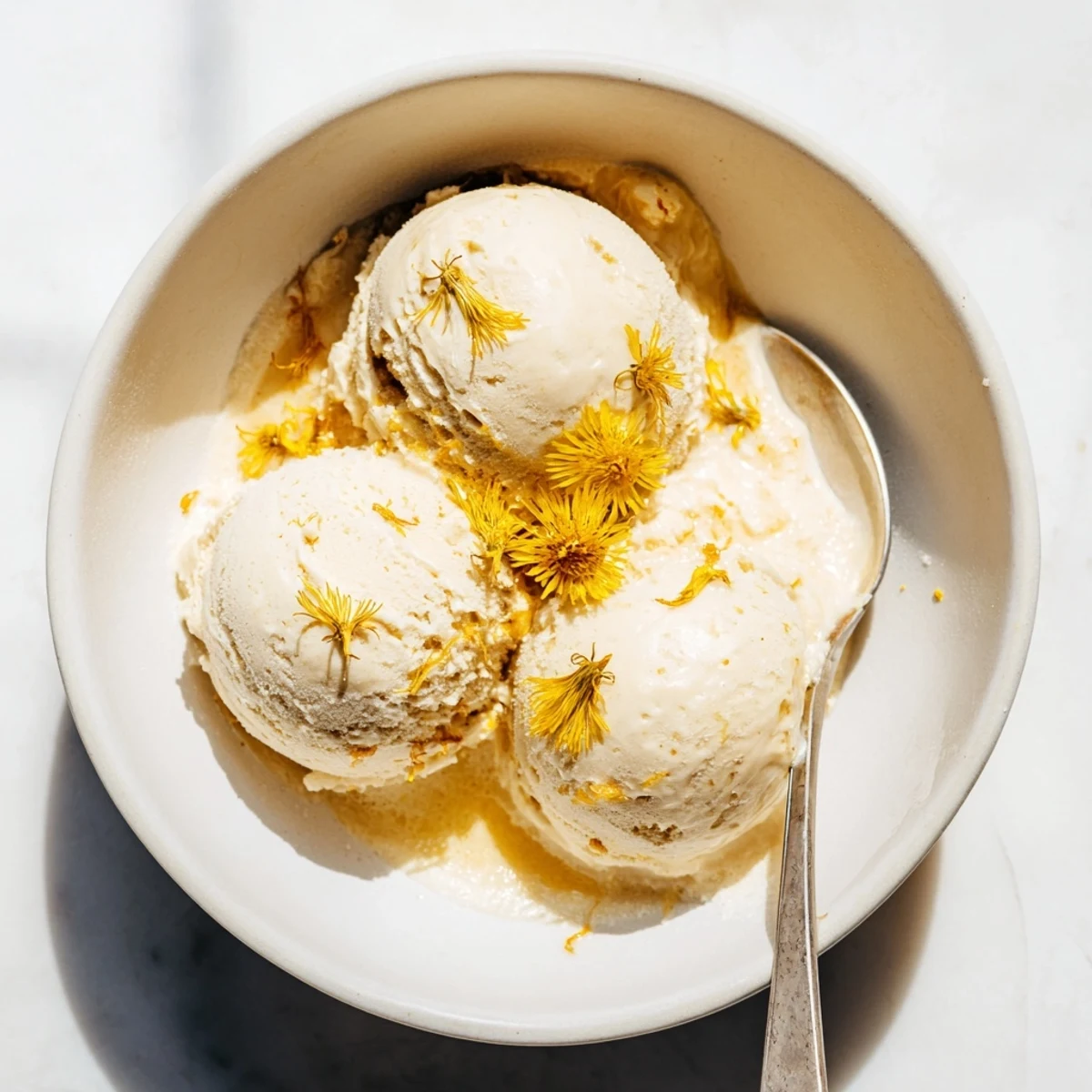Creamy dandelion honey ice cream scooped into a bowl topped with golden honey drizzle