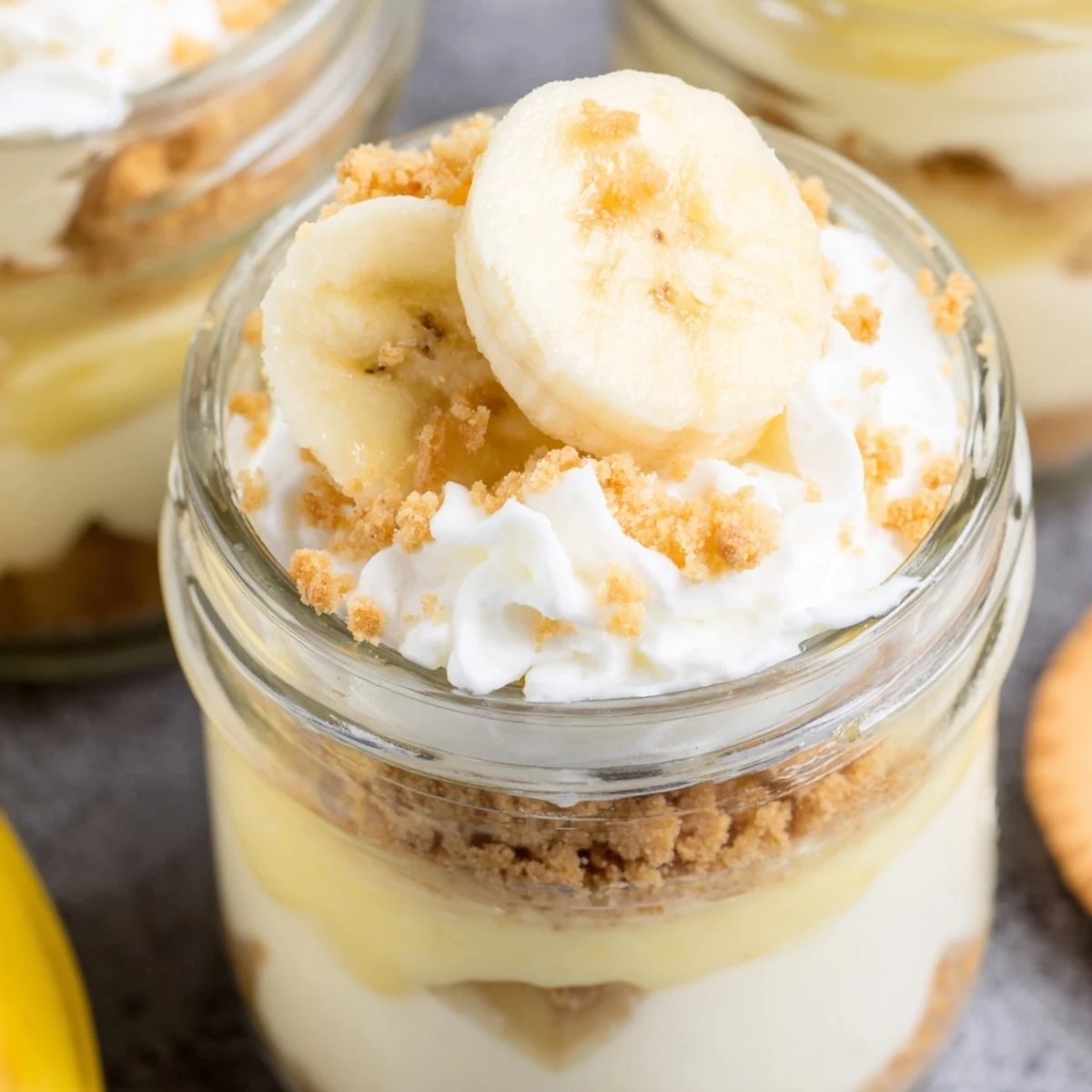 Individual banana pudding cheesecake cups topped with golden wafer crumbs and fresh banana rounds