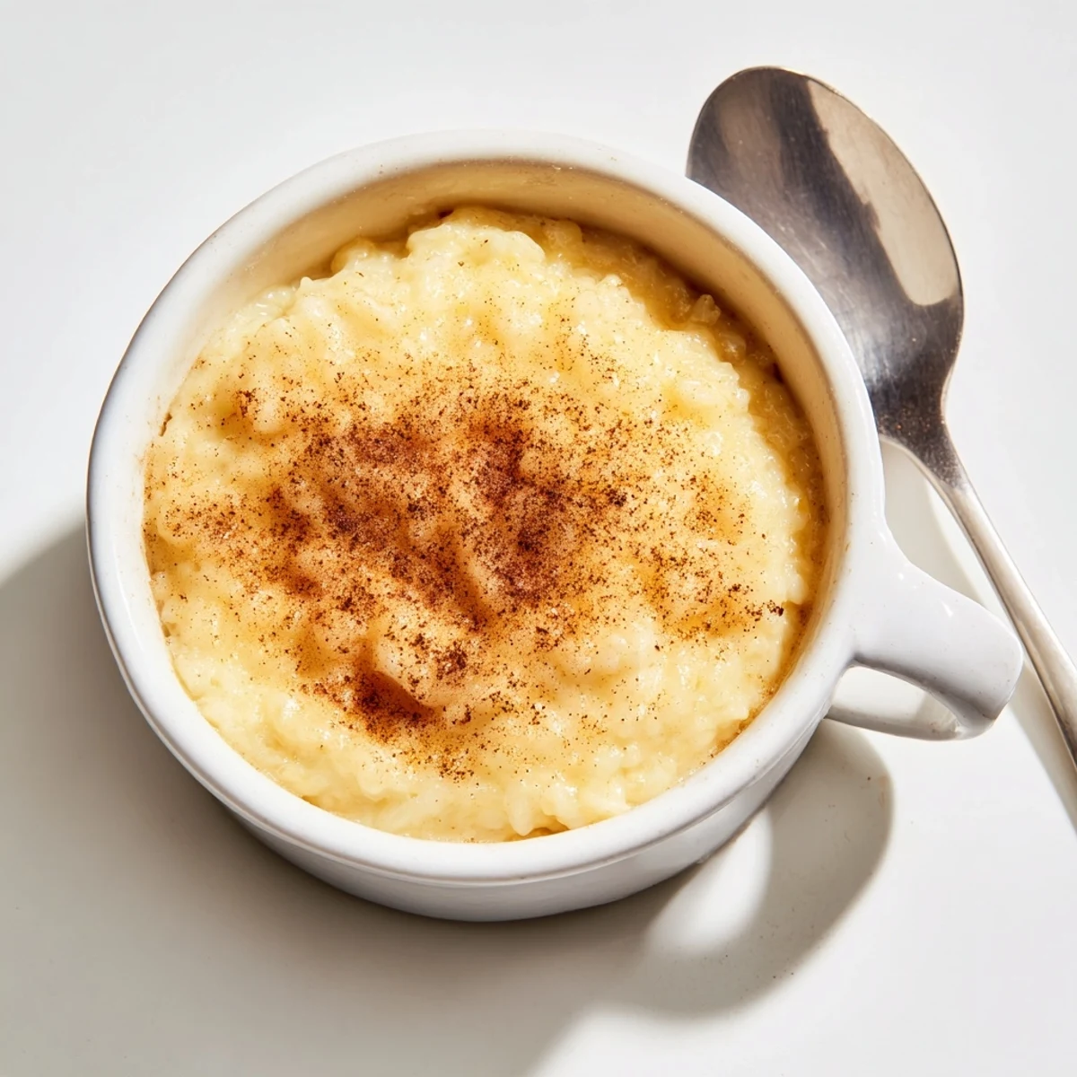 Creamy Portuguese rice custard in white ramekins topped with golden cinnamon sprinkled sugar crust