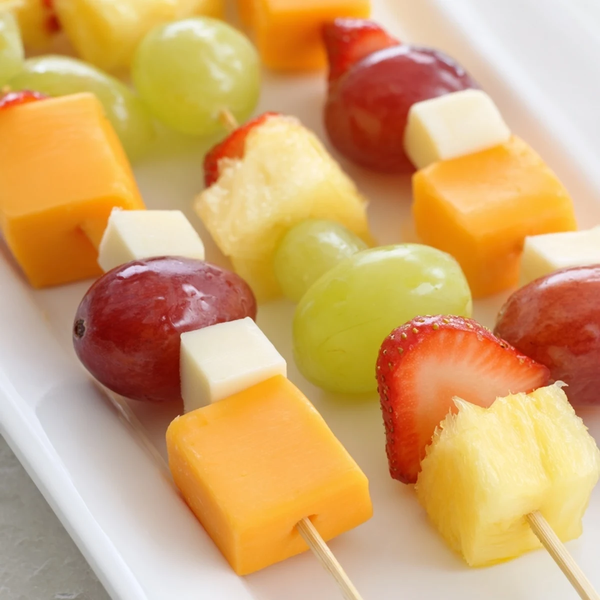 Colorful fruit and cheese kabobs arranged on a platter with fresh mint garnish