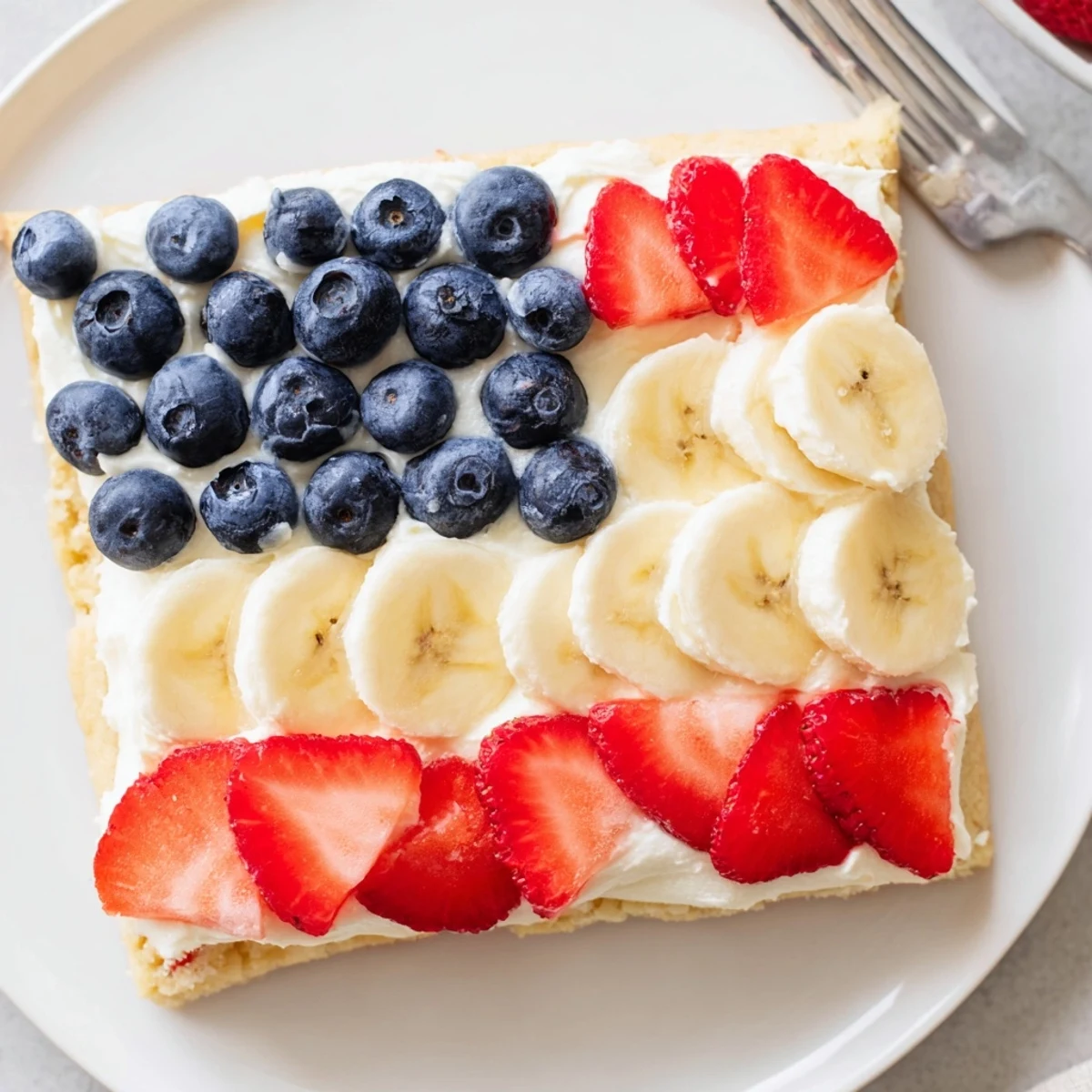 A slice of American Flag Fruit Pizza shows juicy strawberries, banana slices, and blueberries