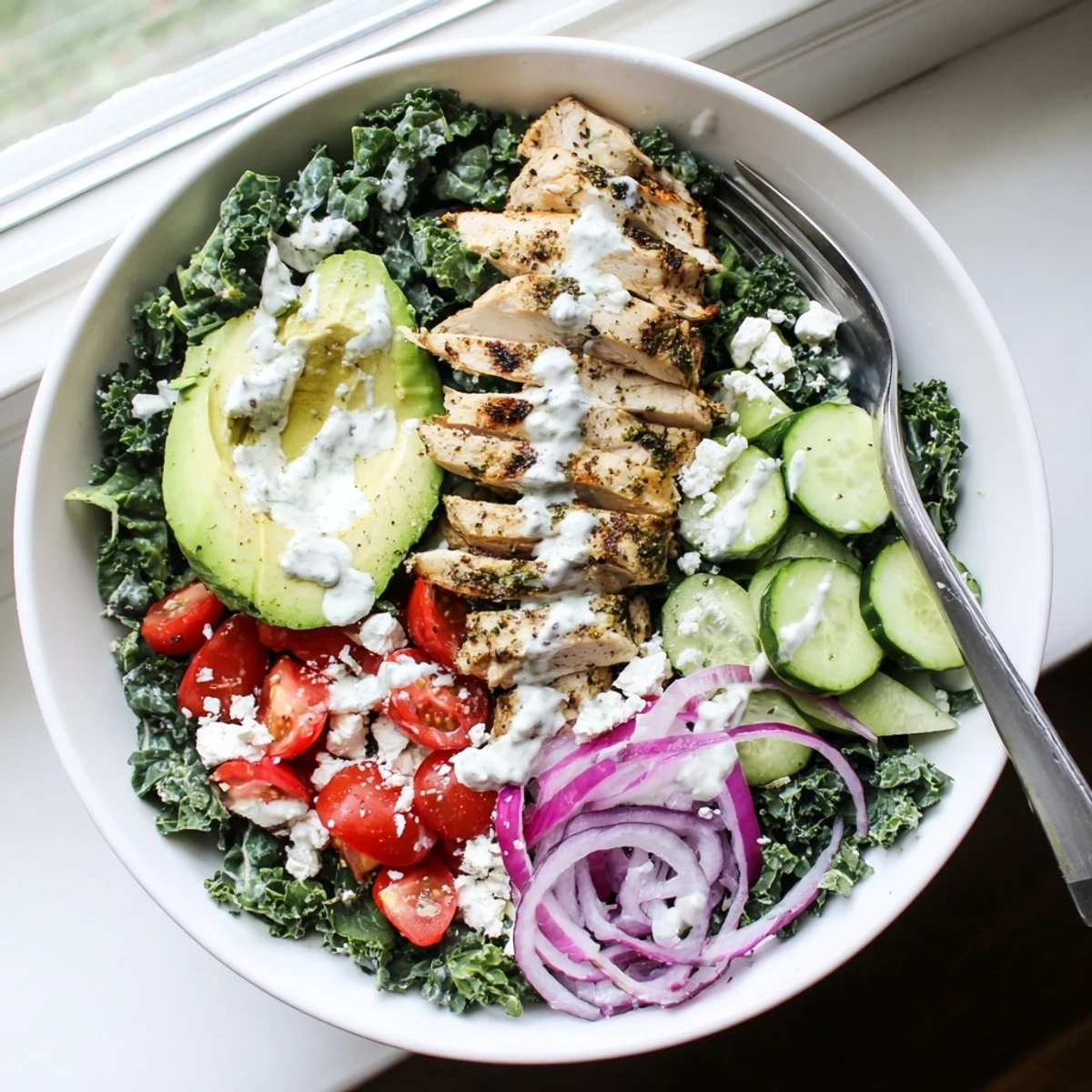 Colorful meal prep bowl featuring marinated kale and chicken with cherry tomatoes cucumber and creamy yogurt dressing