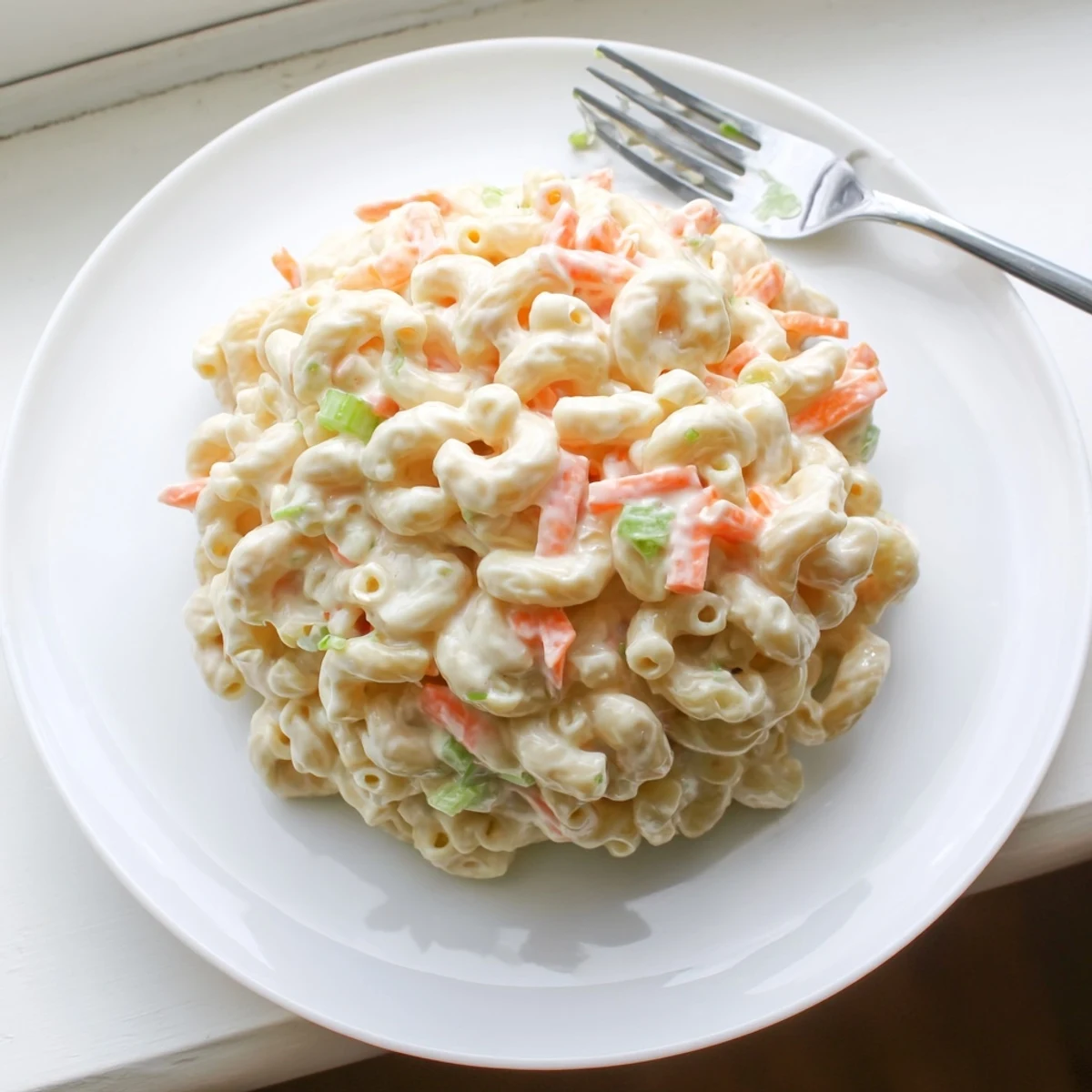 Close up of Hawaiian style mac salad showing smooth texture with carrot flecks and green onion garnish