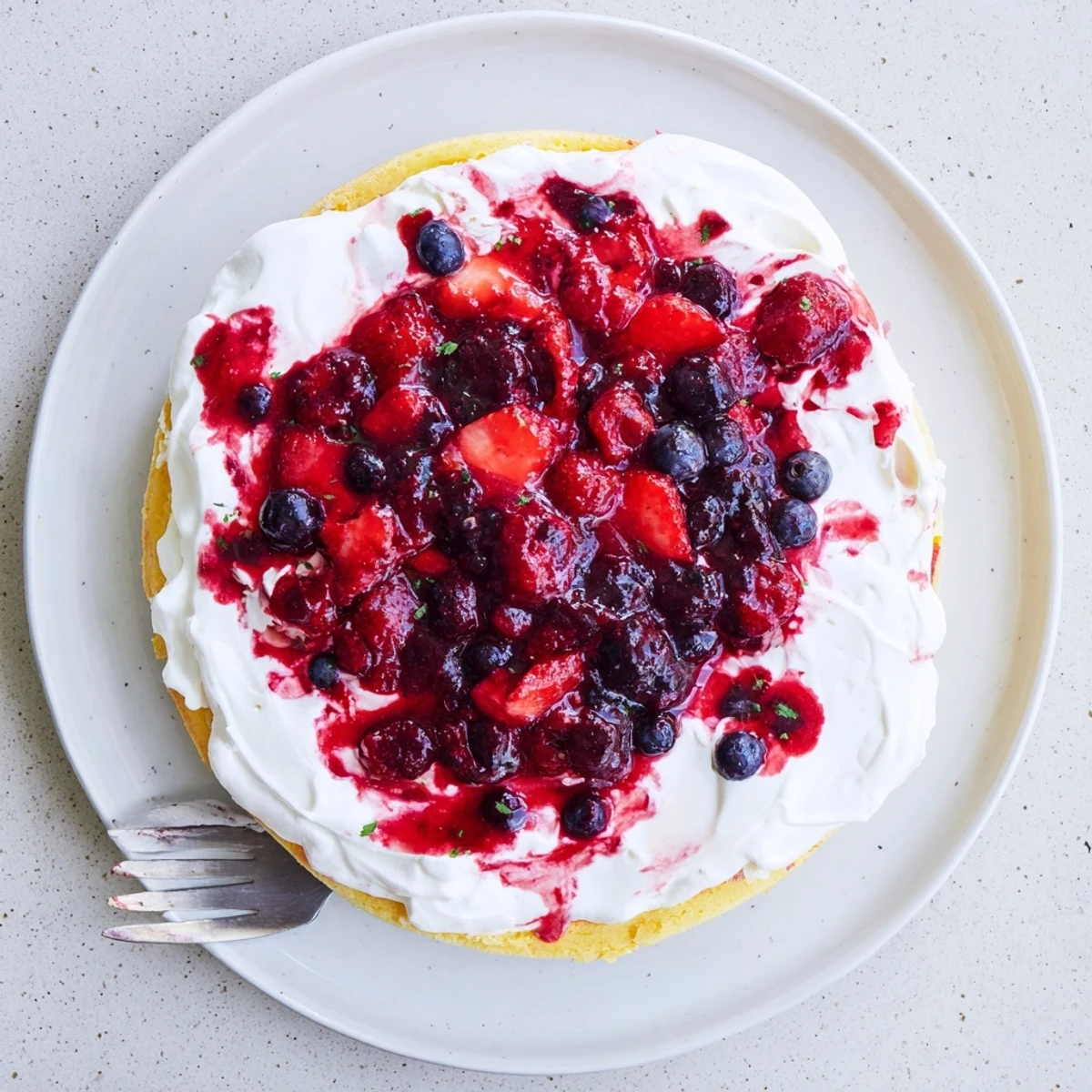 Slice of basil berry cake featuring fresh berries and creamy basil frosting on white plate