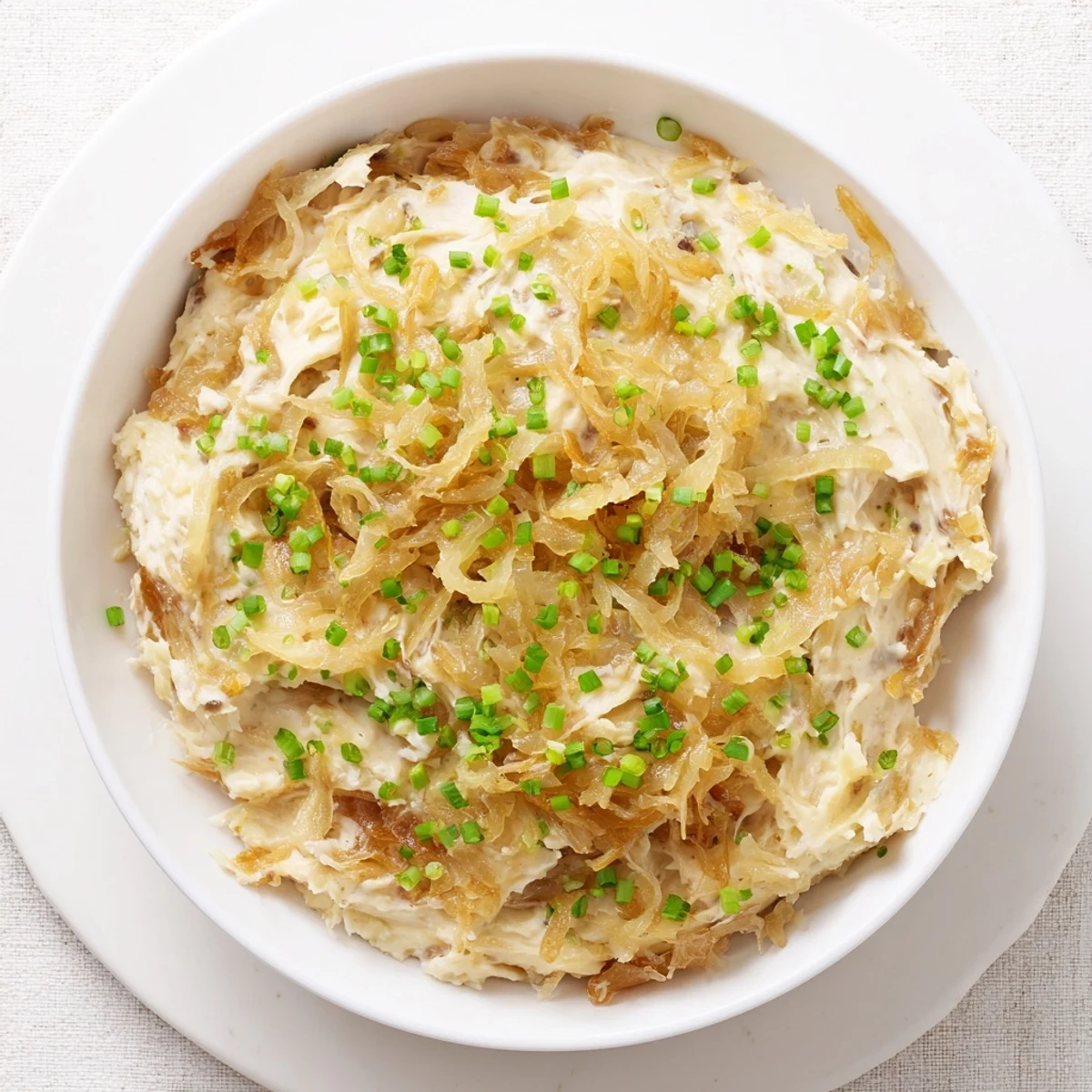 Creamy French onion dip topped with caramelized onions and fresh green onion garnish in a white serving bowl