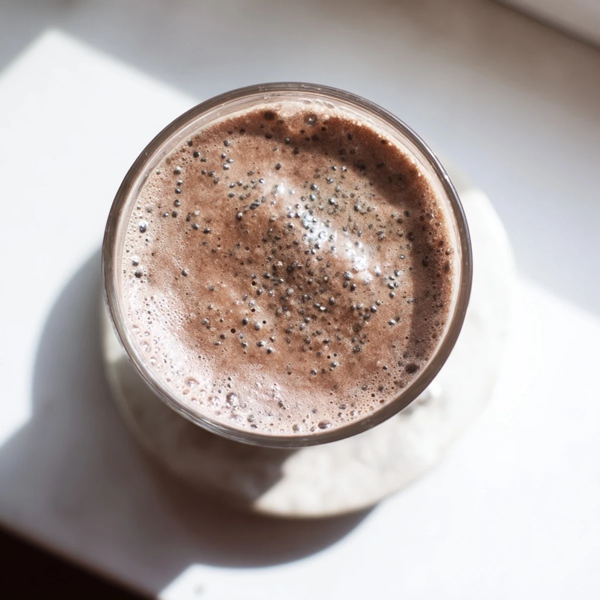 Glass of nourishing raw chocolate banana shake topped with cacao nibs and coconut flakes for added crunch