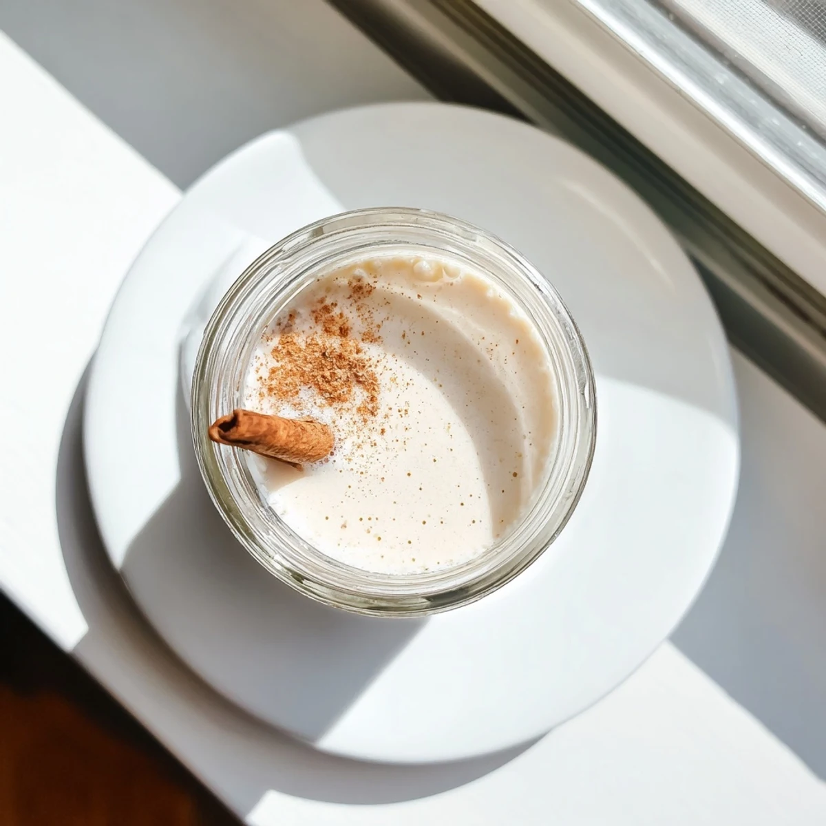 Creamy white homemade almond milk poured into clear glass beside whole raw almonds