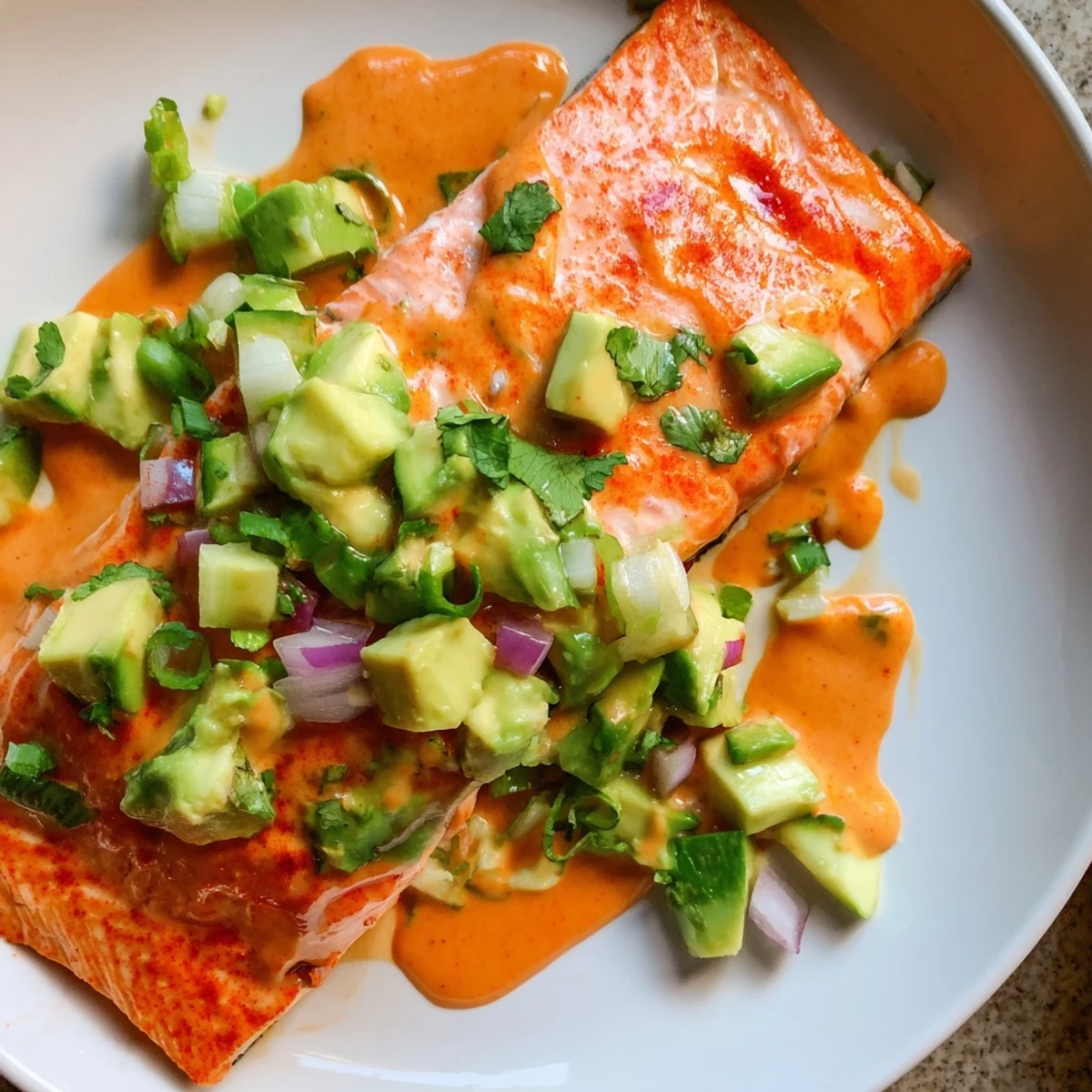 Perfectly roasted bang bang salmon drizzled with sweet chili sauce over cool avocado cucumber salsa
