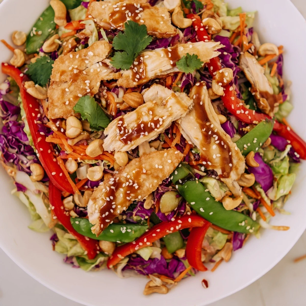 Golden sliced chicken over purple cabbage and roasted cashews in a tangy vibrant bowl