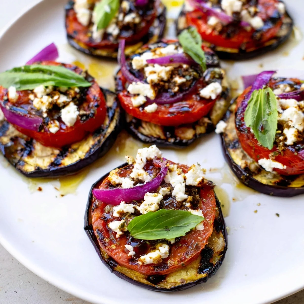 Smoky grilled tomato eggplant stacked on a platter with fresh basil and crumbled feta