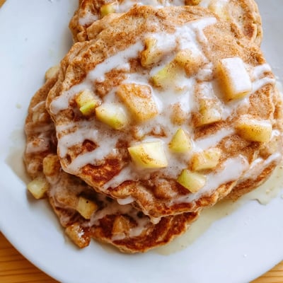 Stack of warm Apple Fritter Pancakes drizzled with sweet glaze, perfect for a weekend breakfast or brunch served with maple syrup.